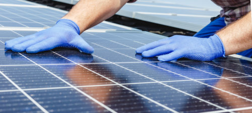 Male worker hands in glows on solar panel, technician installing solar panels